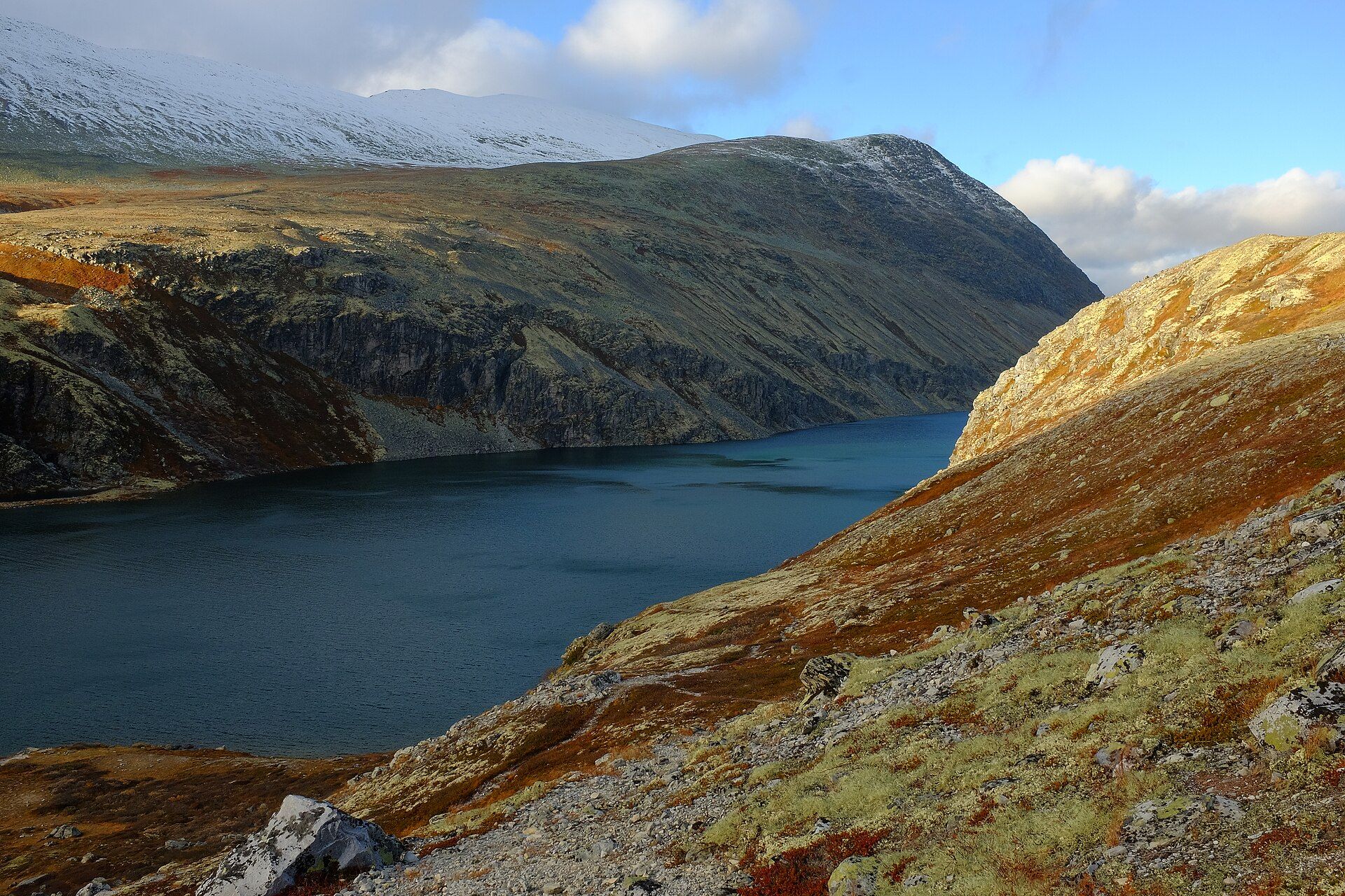 Rondvatnet lake between rust-coloured slopes and snow-capped peaks in Rondane