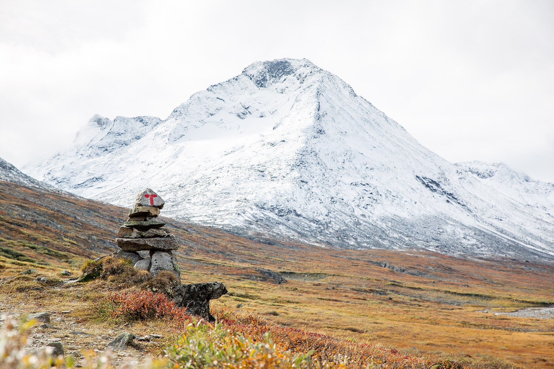 A cairn with a red T in Visdalen, Jotunheimen, with a snow-covered peak and red autumn heath