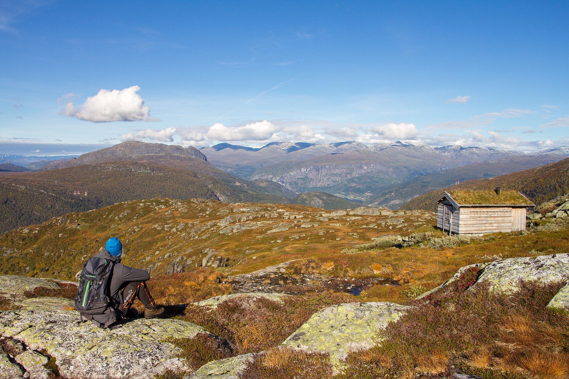 Hiker resting on rocks by a turf-roofed hut on the golden plateau above Granvin in Hardanger