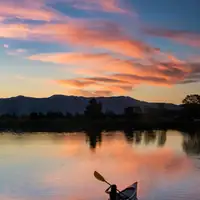 A lone canoeist paddles peacefully on a serene lake during a vibrant sunset.