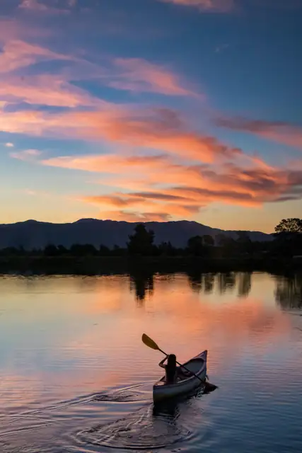 A lone canoeist paddles peacefully on a serene lake during a vibrant sunset.