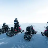 A group of tourists on snowmobiles explore the vast Arctic landscape under clear skies.