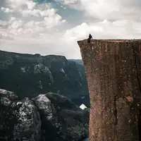 A daring traveler sits on the edge of Preikestolen, overlooking breathtaking Norwegian fjords.