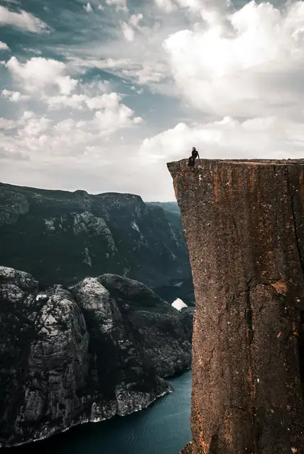 A daring traveler sits on the edge of Preikestolen, overlooking breathtaking Norwegian fjords.