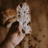 Artistic close-up of a rustic bread slice held by a hand with blurred background.