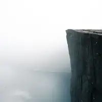 Two people stand on the edge of the famous Preikestolen cliff shrouded in fog, overlooking Lysefjord in Norway.