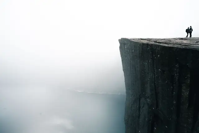 Two people stand on the edge of the famous Preikestolen cliff shrouded in fog, overlooking Lysefjord in Norway.
