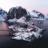 A stunning aerial view of Hamnøy, Norway, showcasing snow-covered mountains and fjords at twilight.