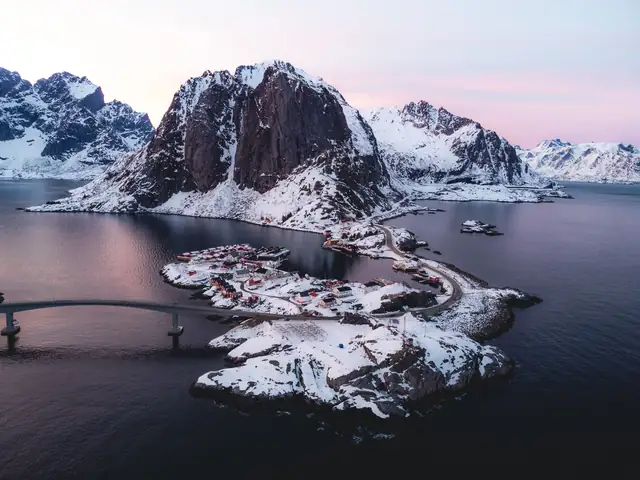 A stunning aerial view of Hamnøy, Norway, showcasing snow-covered mountains and fjords at twilight.
