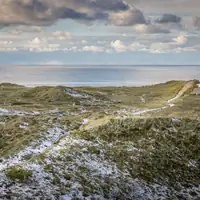 Snow-dusted dunes overlooking the North Sea under cloudy skies in Agger, Denmark.