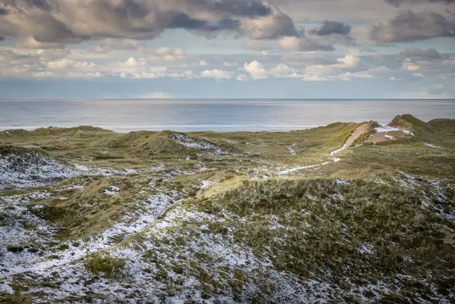 Snow-dusted dunes overlooking the North Sea under cloudy skies in Agger, Denmark.
