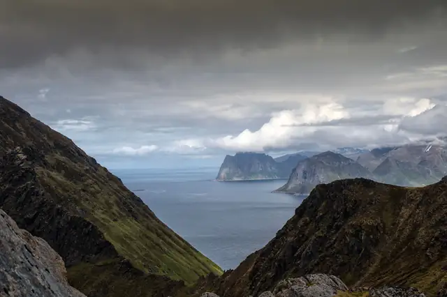 A stunning view of the Lofoten fjord surrounded by rocky mountains and a dramatic cloudy sky.